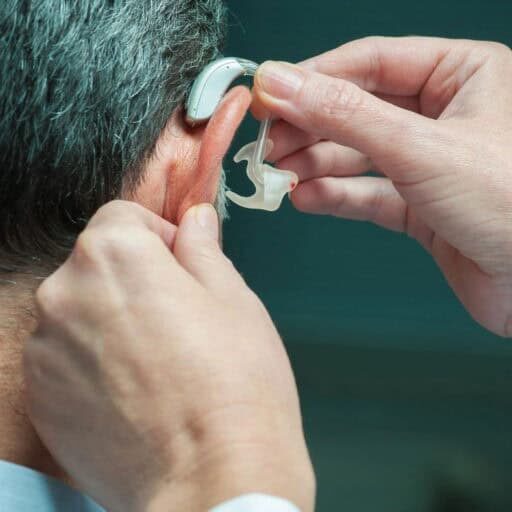 Doctor inserting hearing aid in man's ear